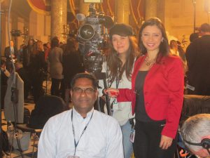 three people, a reporter, producer and a camerman in the rotunda, smile for the camera