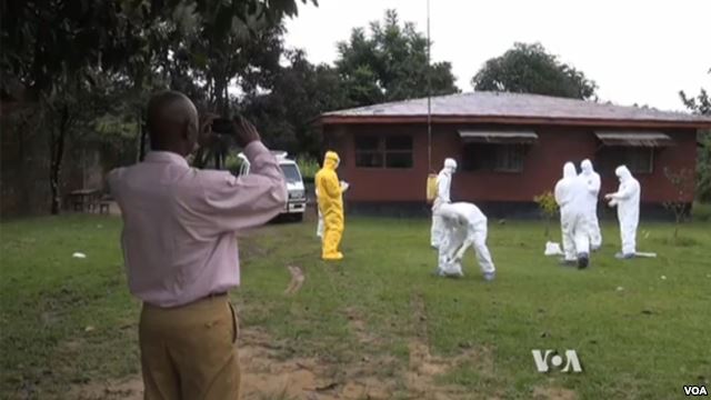 Man takes photo of health workers cleaning up in a grassy area by a home.