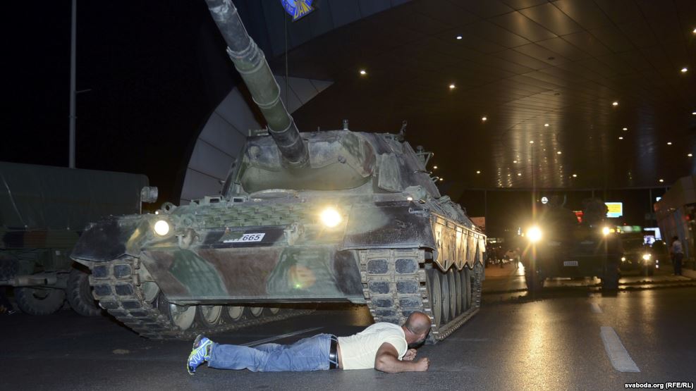 Man lies on the street in front of a tank at night